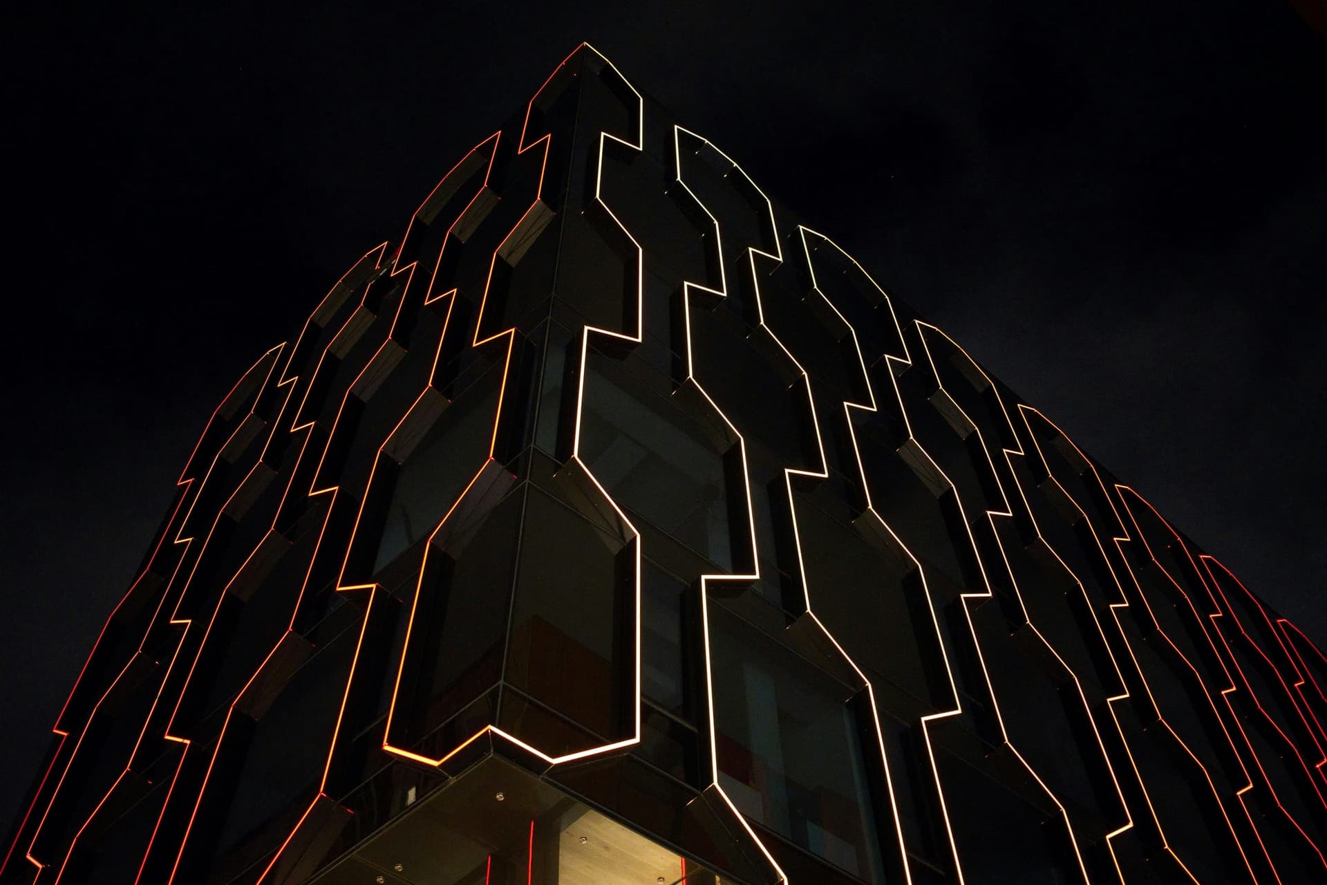 A dark tower traced in lines of orange light at night